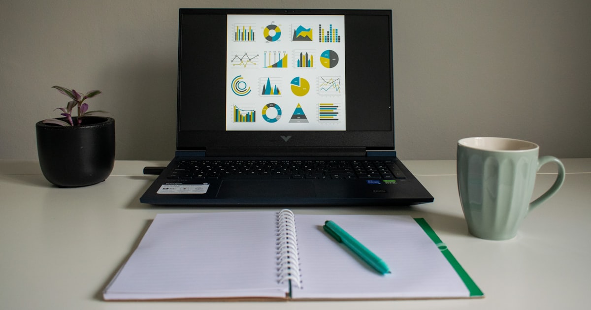 Laptop showing financial charts on a clean desk with notebook and coffee — website cost planning